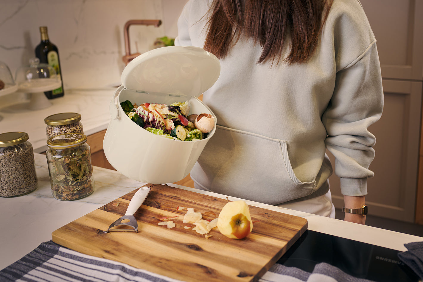 Person hält in der Küche den geöffneten Organko Daily in Cremeweiß, gefüllt mit Obst- und Gemüseresten.