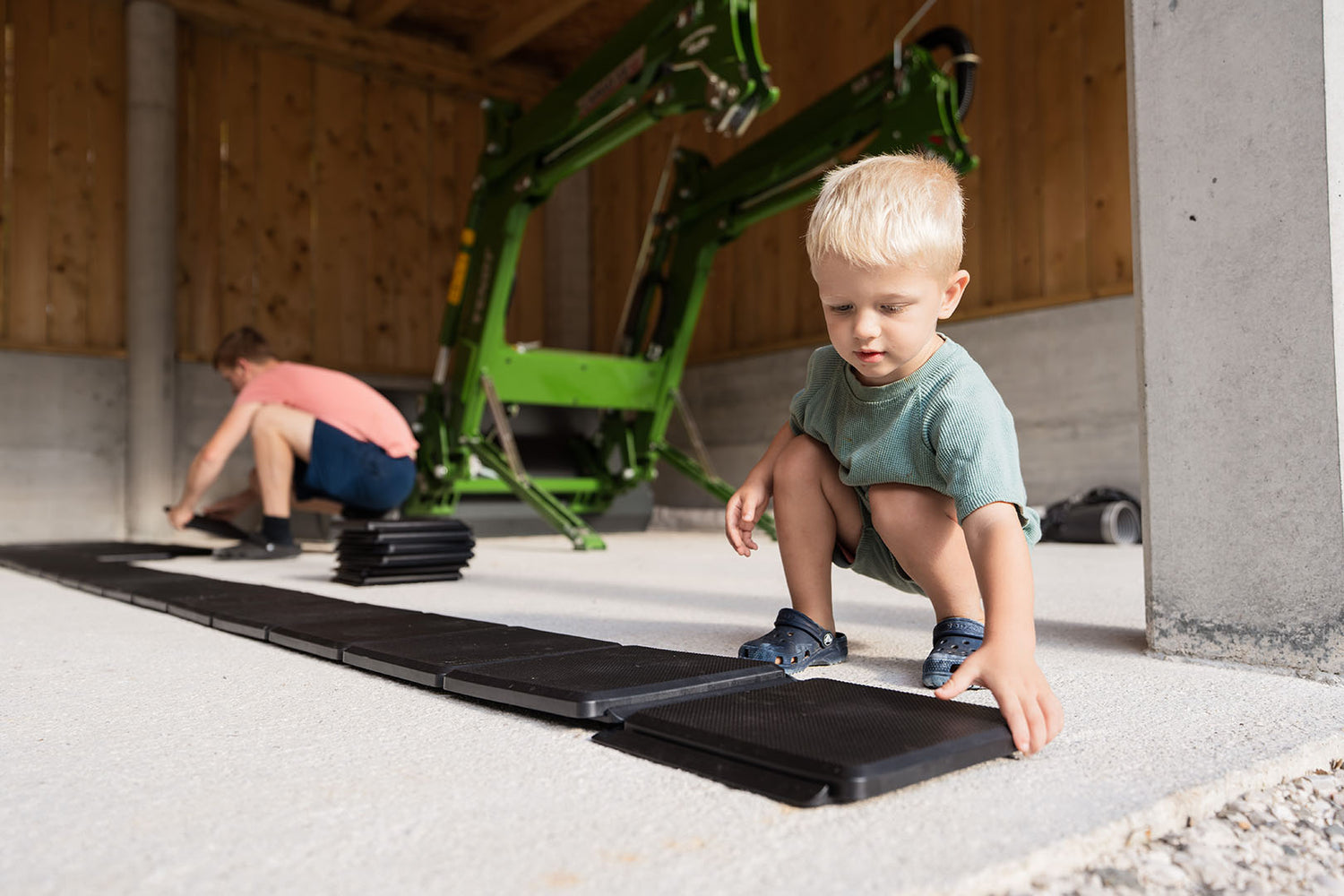 Ein kleines Kind hilft, Gehplatten auf den Betonboden in der Garage zu verlegen.