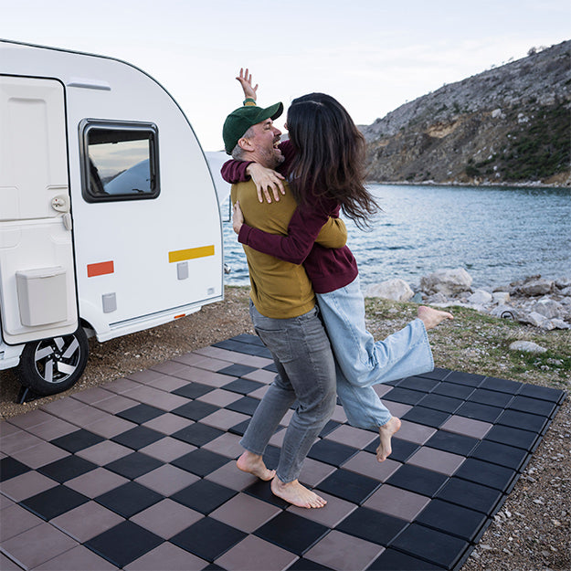 Barfuß tanzendes Paar auf Skaza Bodenplatten vor dem Wohnwagen – perfekte Lösung für Camping mit Komfort und Stil