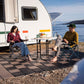 Zwei Personen sitzen barfuß auf Skaza begehbaren Bodenplatten vor einem Wohnwagen – perfekte Lösung für Camping und Outdoor-Bereiche