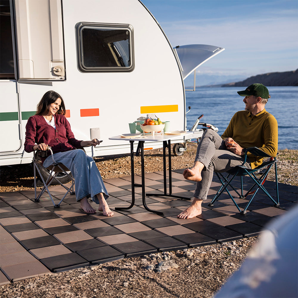 Zwei Personen sitzen barfuß auf Skaza begehbaren Bodenplatten vor einem Wohnwagen – perfekte Lösung für Camping und Outdoor-Bereiche