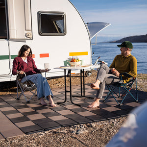 Zwei Personen sitzen barfuß auf Skaza begehbaren Bodenplatten vor einem Wohnwagen – perfekte Lösung für Camping und Outdoor-Bereiche